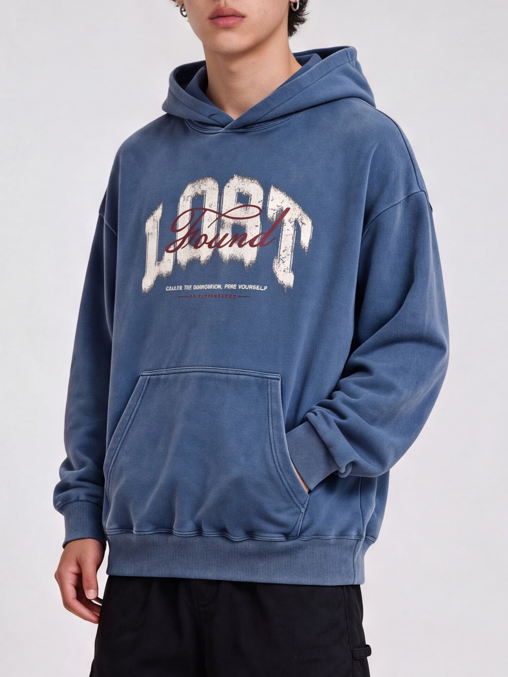 Three-quarter view of a blue Lost & Found washed hoodie with a hand in the kangaroo pocket.